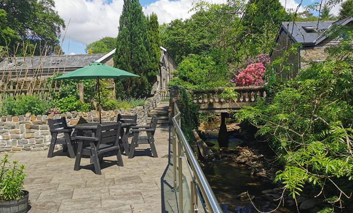Black outdoor dining set on a paved terrace beside a stream, surrounded by stone walls and greenery